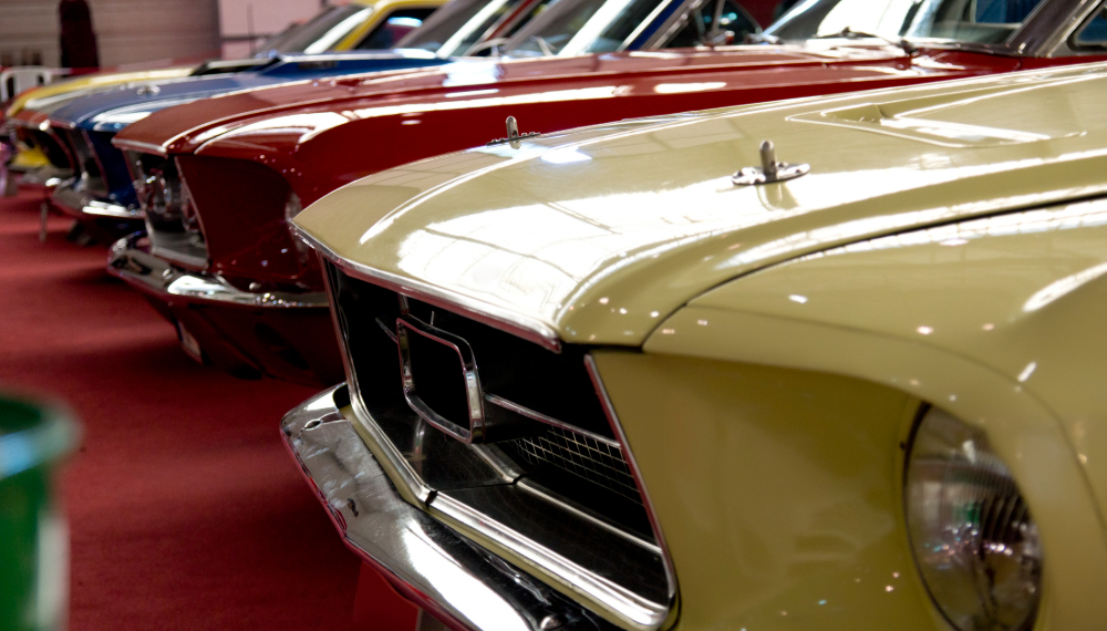 Row of yellow, red, and blue classic muscle cars lined up on a red carpet